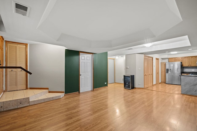 unfurnished living room featuring light wood-type flooring and a tray ceiling