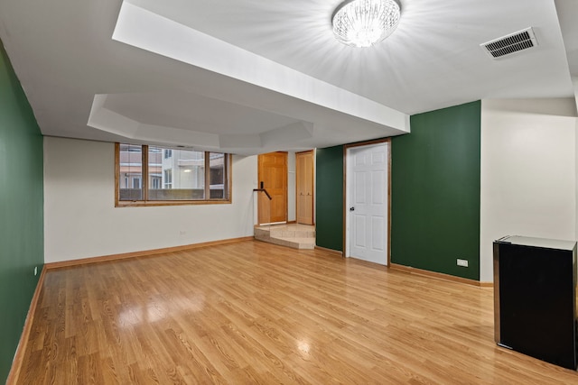 unfurnished living room featuring an inviting chandelier, light hardwood / wood-style flooring, and a tray ceiling