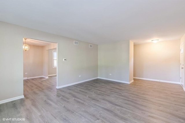 spare room with light wood-type flooring and an inviting chandelier