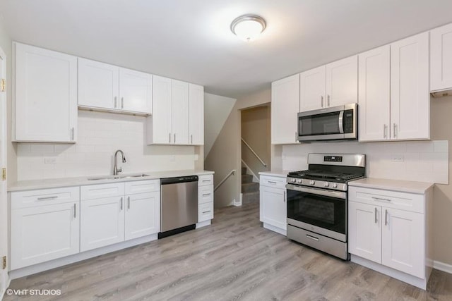 kitchen with appliances with stainless steel finishes, light wood-type flooring, tasteful backsplash, sink, and white cabinetry