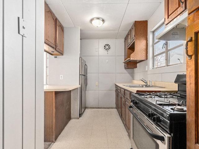 kitchen with range with gas stovetop, stainless steel refrigerator, tile walls, and sink