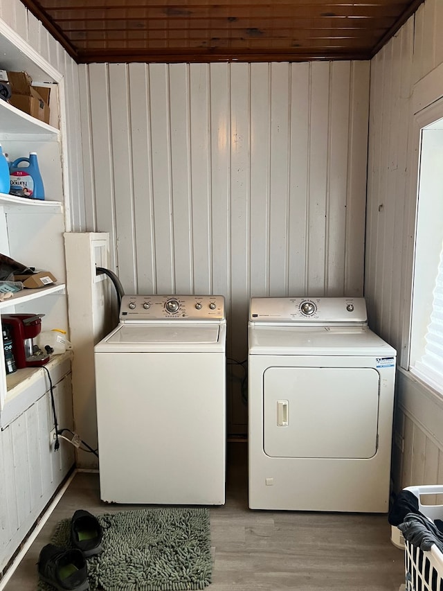 laundry area featuring light wood-type flooring, wooden walls, and washing machine and clothes dryer