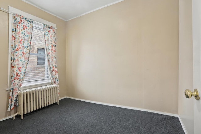 spare room featuring radiator heating unit, dark colored carpet, baseboards, and crown molding