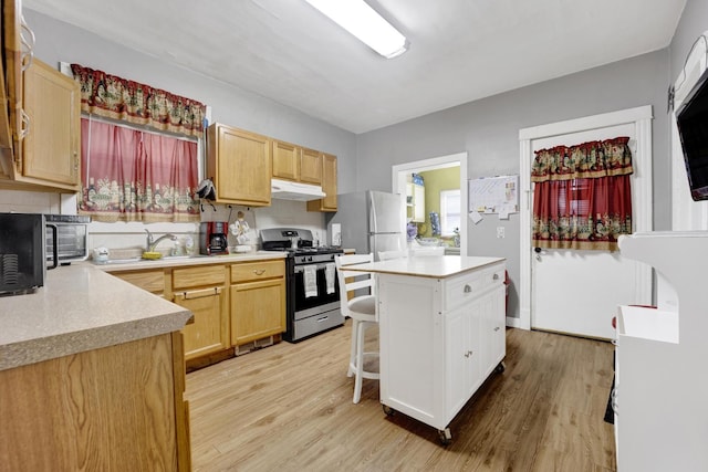 kitchen with sink, a center island, a kitchen breakfast bar, stainless steel gas range oven, and light hardwood / wood-style floors