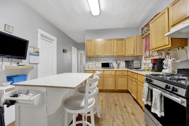 kitchen with a center island, light brown cabinets, stainless steel range with gas cooktop, tasteful backsplash, and a breakfast bar area