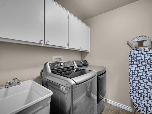 clothes washing area with dark hardwood / wood-style floors, cabinets, washing machine and clothes dryer, and sink