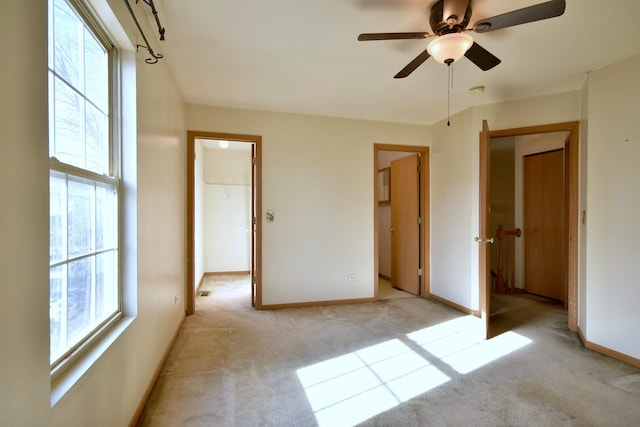 unfurnished bedroom featuring a walk in closet, light colored carpet, a closet, and ceiling fan