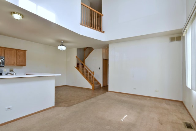 unfurnished living room featuring light carpet and a towering ceiling