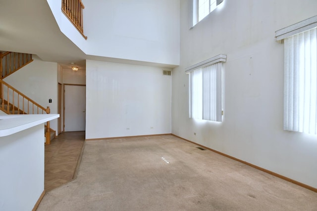 unfurnished living room featuring a towering ceiling and light colored carpet