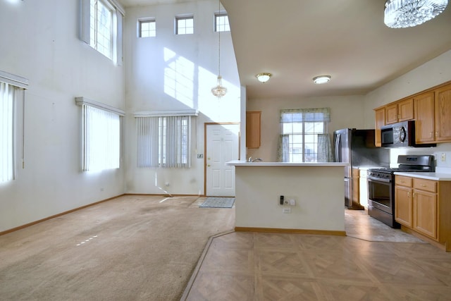 kitchen with light colored carpet, stainless steel appliances, hanging light fixtures, and a high ceiling