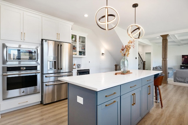 kitchen with hanging light fixtures, appliances with stainless steel finishes, light hardwood / wood-style floors, white cabinetry, and decorative columns