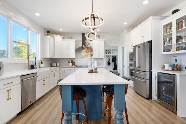 kitchen with beverage cooler, wall chimney range hood, decorative backsplash, white cabinets, and appliances with stainless steel finishes