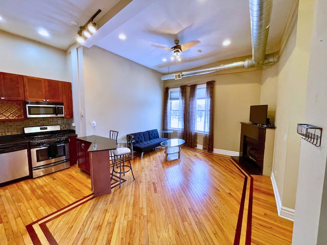 kitchen featuring a kitchen bar, backsplash, stainless steel appliances, and light hardwood / wood-style flooring