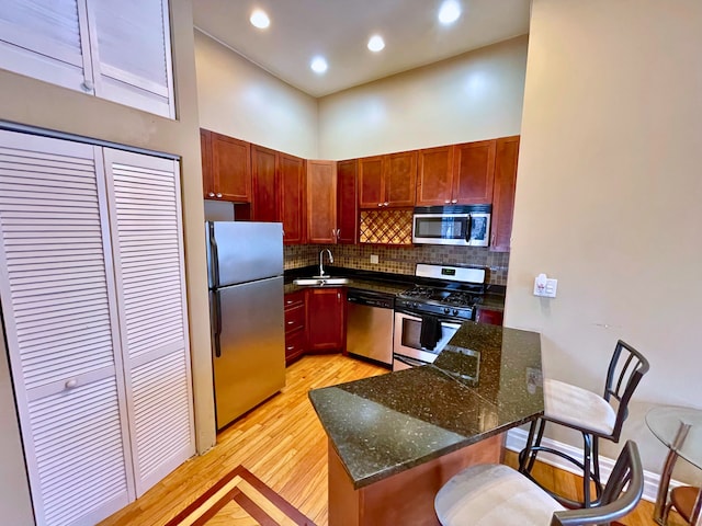 kitchen with a kitchen bar, appliances with stainless steel finishes, a towering ceiling, dark stone counters, and sink