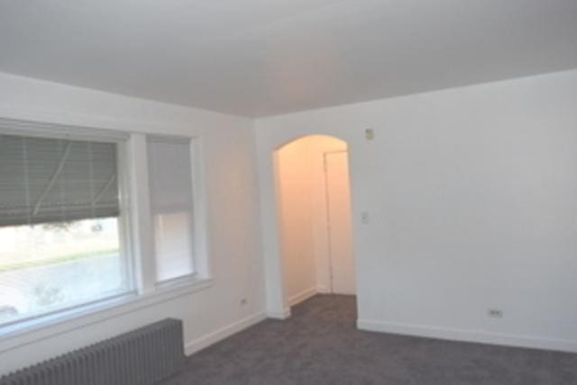 empty room featuring radiator and dark colored carpet