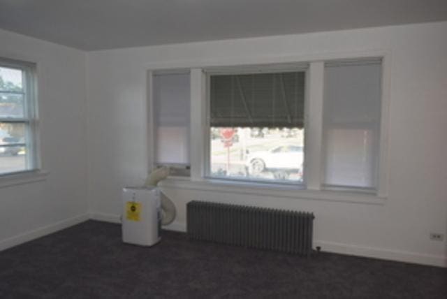 spare room featuring radiator and dark colored carpet