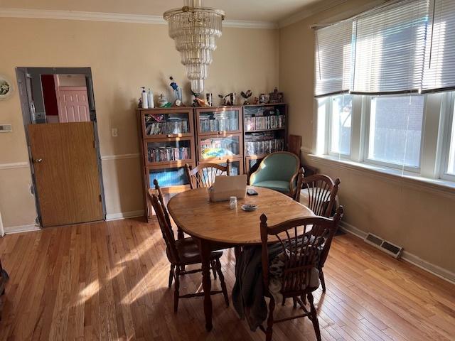 dining space with hardwood / wood-style floors, crown molding, and an inviting chandelier