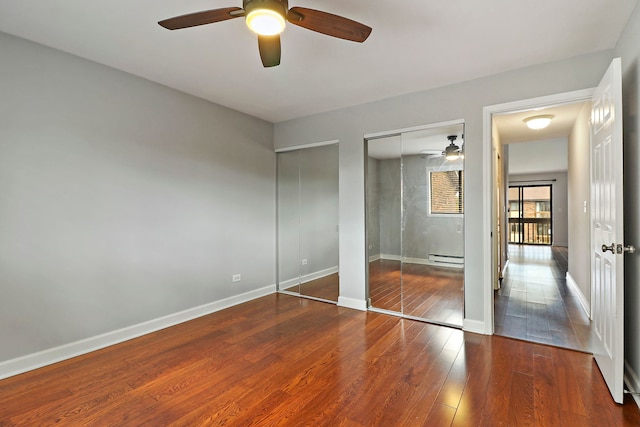 unfurnished bedroom featuring a baseboard heating unit, two closets, wood-type flooring, and ceiling fan