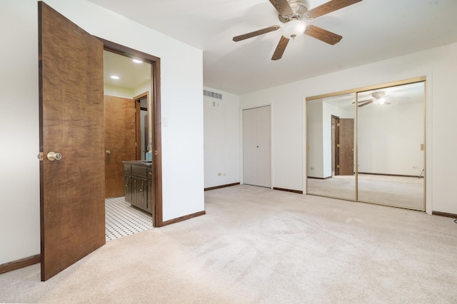 unfurnished bedroom featuring ceiling fan, light colored carpet, and ensuite bath