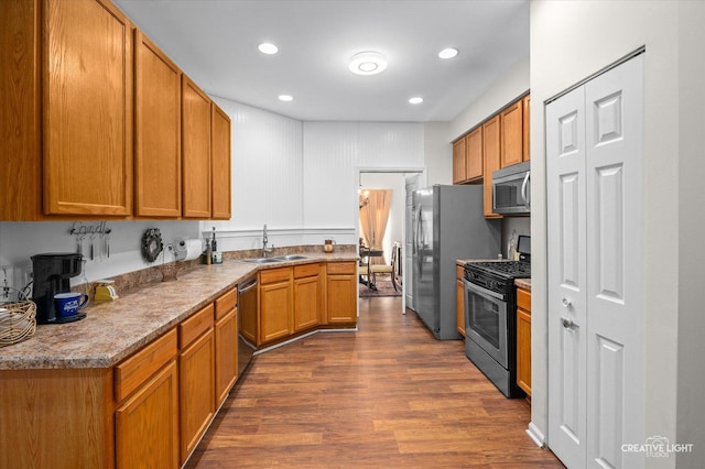 kitchen with appliances with stainless steel finishes, dark hardwood / wood-style floors, light stone counters, and sink