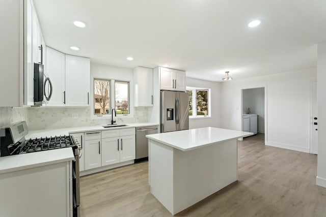 kitchen with light wood-type flooring, stainless steel appliances, sink, white cabinets, and a center island