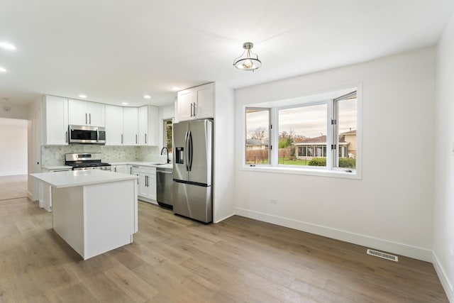 kitchen with pendant lighting, white cabinets, sink, appliances with stainless steel finishes, and a kitchen island