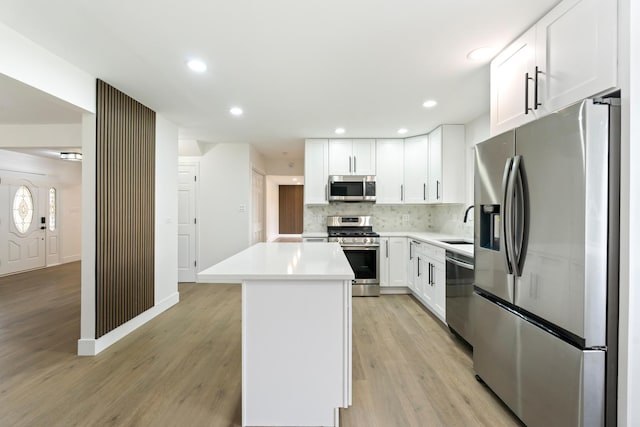 kitchen with light hardwood / wood-style flooring, tasteful backsplash, a kitchen island, white cabinetry, and stainless steel appliances