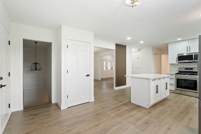 kitchen with backsplash, white cabinets, light hardwood / wood-style flooring, a kitchen island, and stainless steel appliances