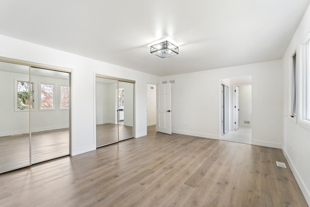 unfurnished bedroom featuring light hardwood / wood-style flooring and multiple closets