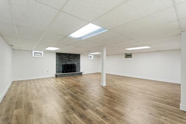 basement with hardwood / wood-style flooring, a drop ceiling, and a brick fireplace