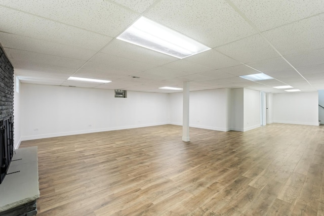 basement featuring hardwood / wood-style floors, a brick fireplace, and a drop ceiling