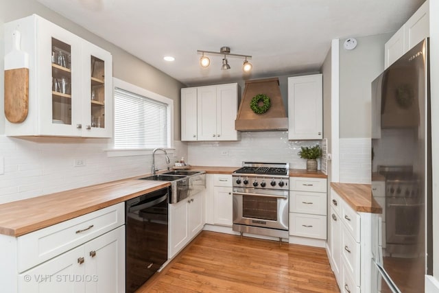 kitchen featuring premium range hood, butcher block countertops, black dishwasher, fridge, and stainless steel range