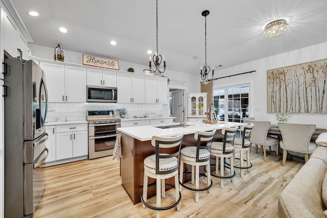 kitchen with a kitchen island with sink, stainless steel appliances, hanging light fixtures, sink, and white cabinetry