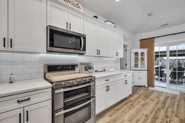 kitchen with stainless steel appliances, white cabinets, tasteful backsplash, and light hardwood / wood-style flooring