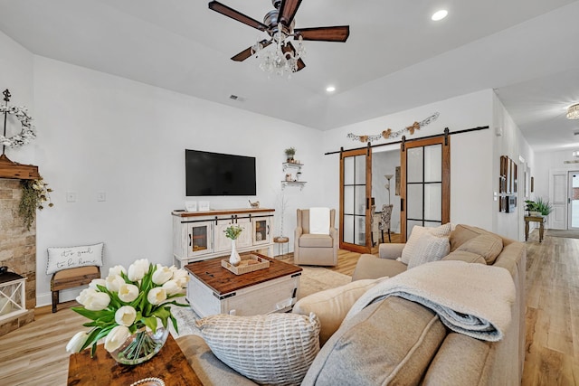 living room with light wood-type flooring, ceiling fan, and a barn door