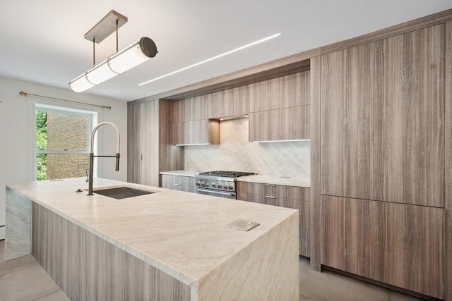 kitchen featuring sink, high end stainless steel range oven, pendant lighting, decorative backsplash, and a center island with sink