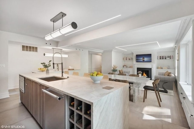 kitchen with built in shelves, sink, a center island with sink, dishwasher, and hanging light fixtures