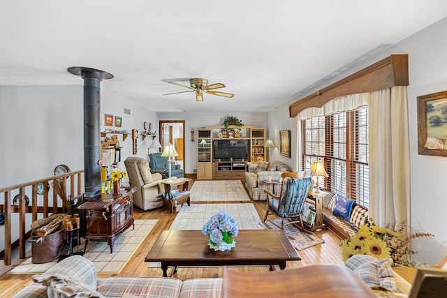 living room with ceiling fan, a wood stove, and light wood-type flooring