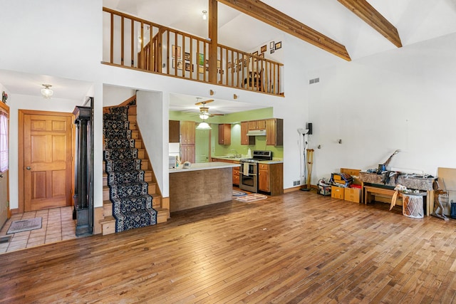 living room featuring light hardwood / wood-style floors, ceiling fan, a high ceiling, beam ceiling, and sink