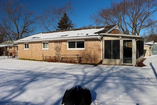 snow covered rear of property with a sunroom