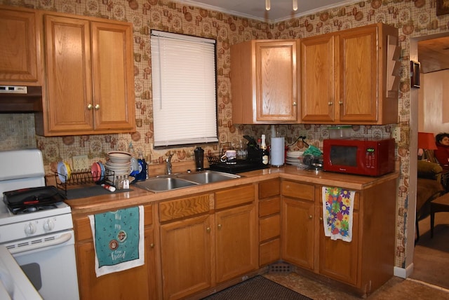 kitchen featuring under cabinet range hood, a sink, light countertops, white gas range, and wallpapered walls