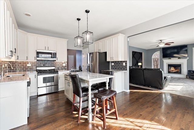 kitchen featuring sink, appliances with stainless steel finishes, white cabinetry, a center island, and decorative light fixtures