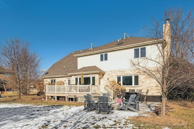 snow covered back of property with a fire pit and a deck