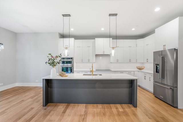 kitchen featuring white cabinets, light wood-type flooring, a kitchen island with sink, and appliances with stainless steel finishes