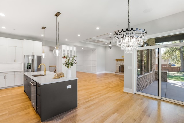 kitchen with sink, a fireplace, an island with sink, stainless steel fridge, and pendant lighting