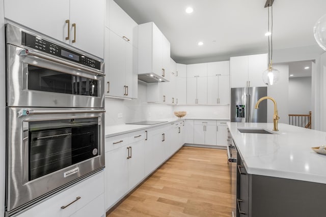 kitchen featuring stainless steel appliances, light wood-type flooring, sink, white cabinetry, and decorative light fixtures