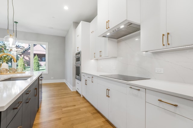 kitchen with hanging light fixtures, black electric stovetop, ventilation hood, sink, and white cabinetry