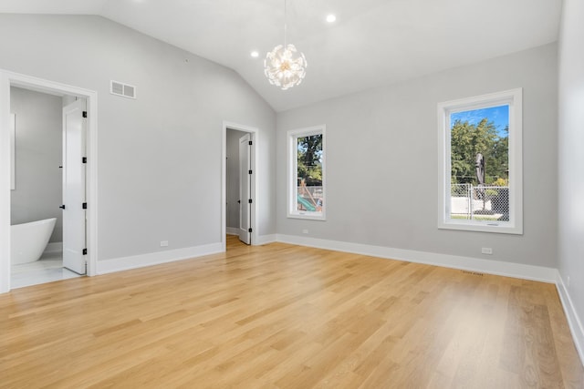 empty room with a notable chandelier, light hardwood / wood-style flooring, and vaulted ceiling