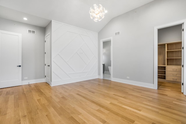 unfurnished bedroom with a closet, light wood-type flooring, a notable chandelier, a walk in closet, and lofted ceiling