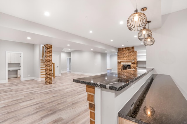 kitchen with decorative light fixtures, ornate columns, light hardwood / wood-style flooring, kitchen peninsula, and a brick fireplace